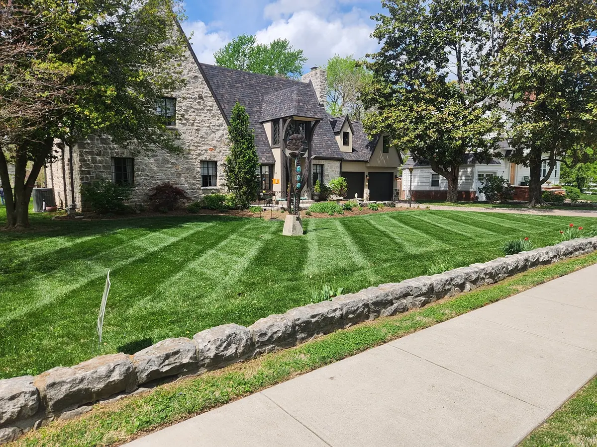 Striped front lawn beside a stone home and low wall
